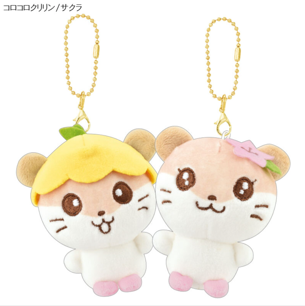 The characters Corocorokuririn and Sakura are shown side by side. A ball chain with a lobster claw hook is attached to the top of their heads. Corocorokuririn has a yellow flower cap with a stem, and Sakura has a pink cherry blossom flower on her ear.